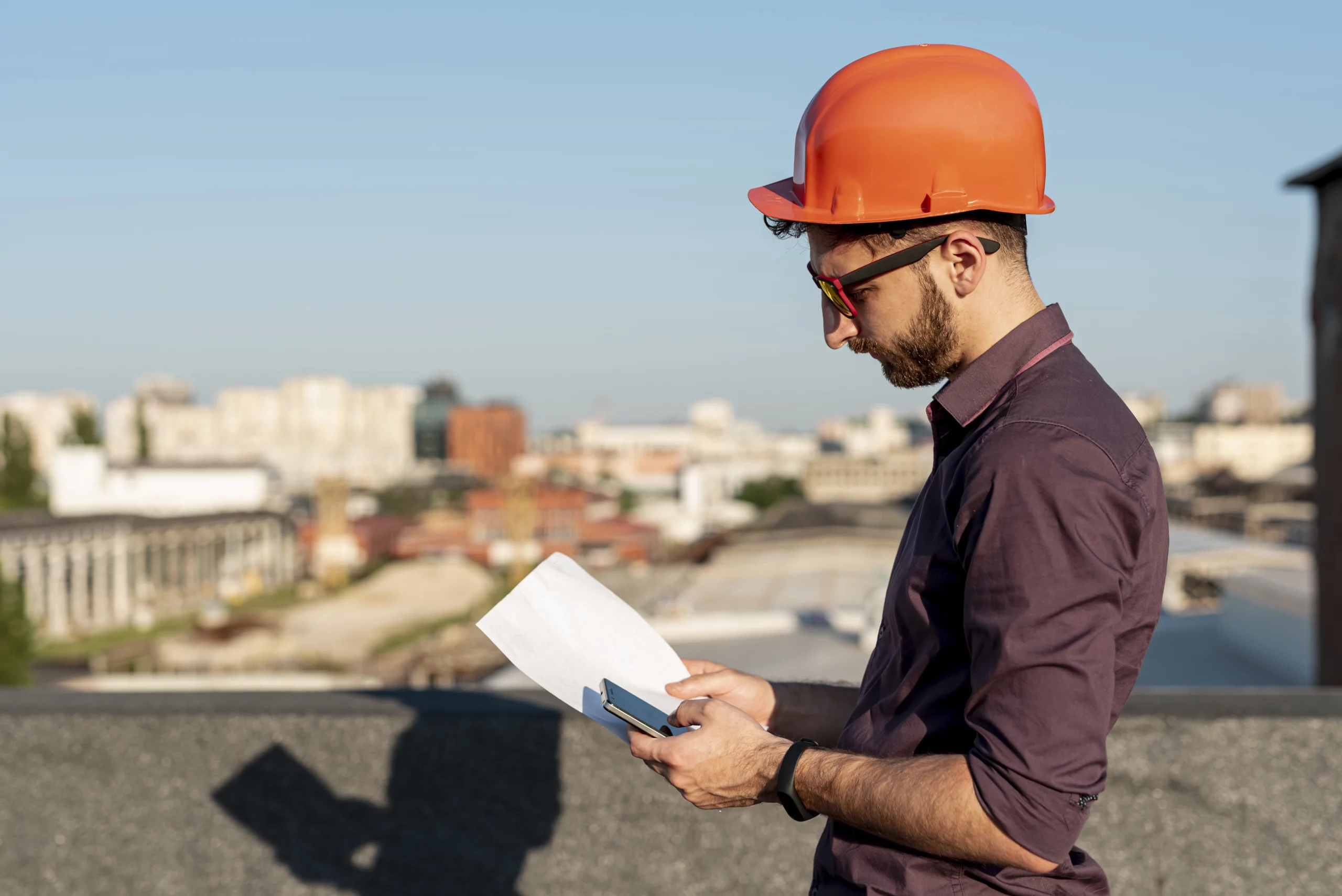 Artisan du bâtiment portant un casque de sécurité orange et consultant des documents sur un chantier