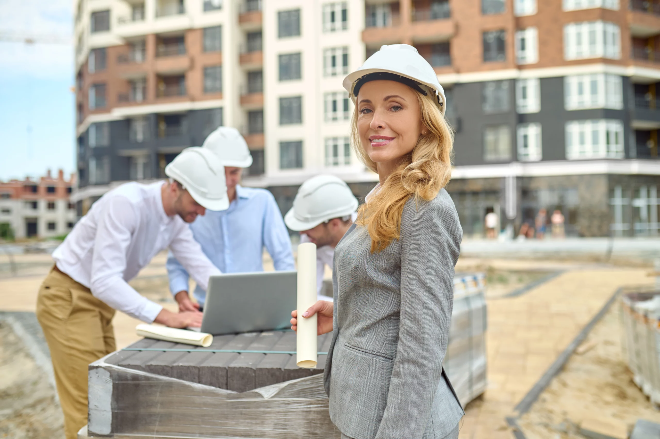 Groupe d'artisans du bâtiment, dont une femme en premier plan, utilisant un ordinateur portable sur un chantier.