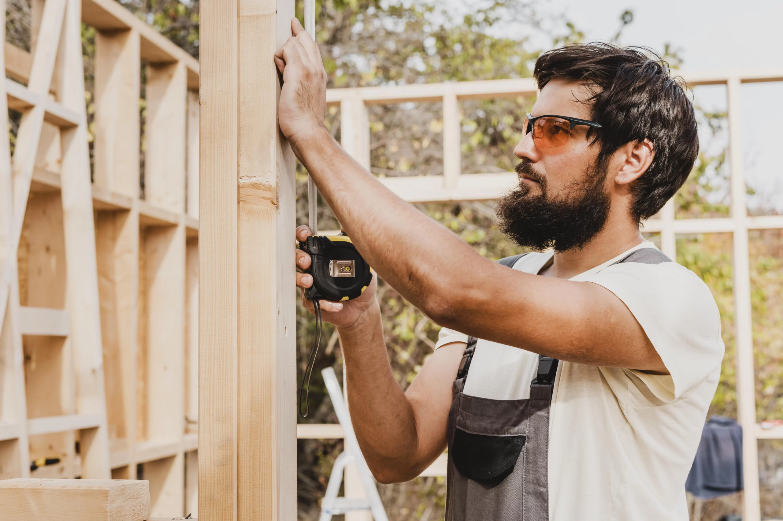 Menuisier utilisant un mètre ruban pour mesurer une structure en bois lors de la construction d'un cadre.